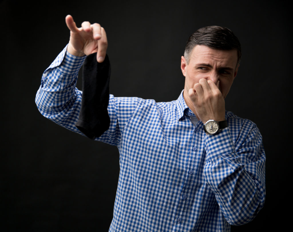 Man holding smelly socks and clogged nose over black background